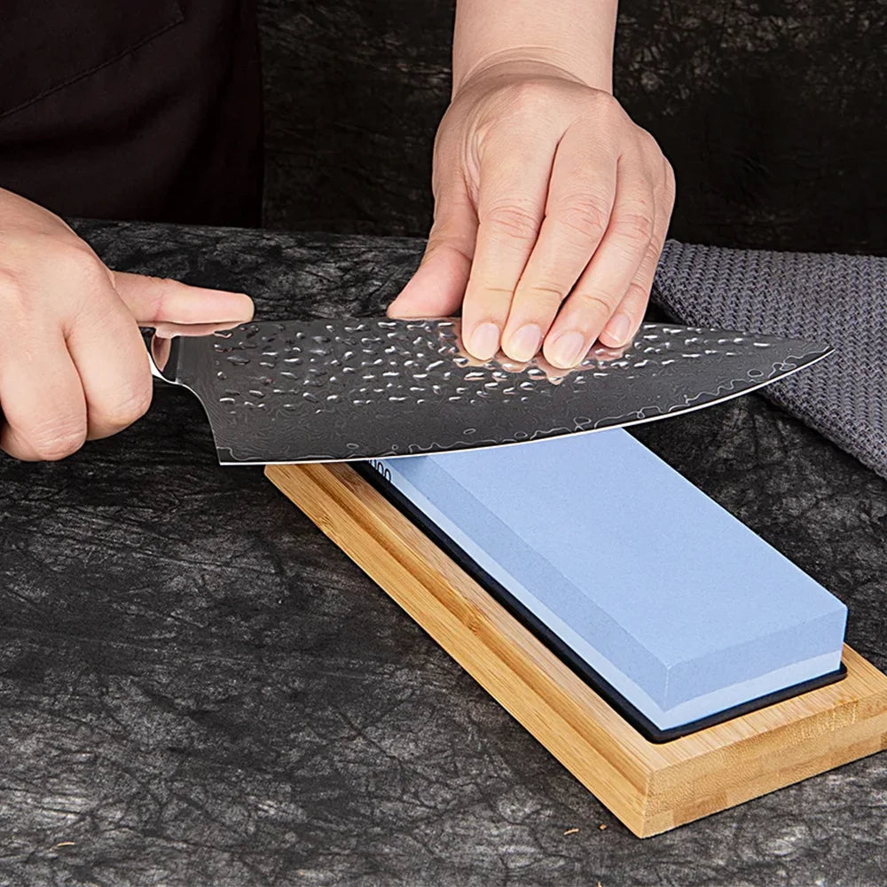 Person sharpening a knife on a whetstone with a wooden holder.