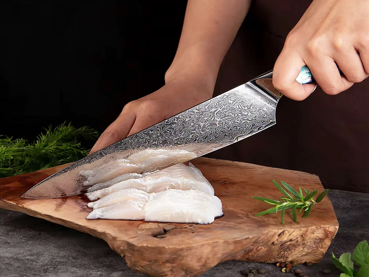 Japanese VG10 Damascus chef knife slicing fresh fish on wooden board with abalone handle